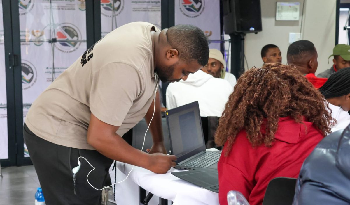 A NIBS facilitator leaning in to help a learner at a laptop.