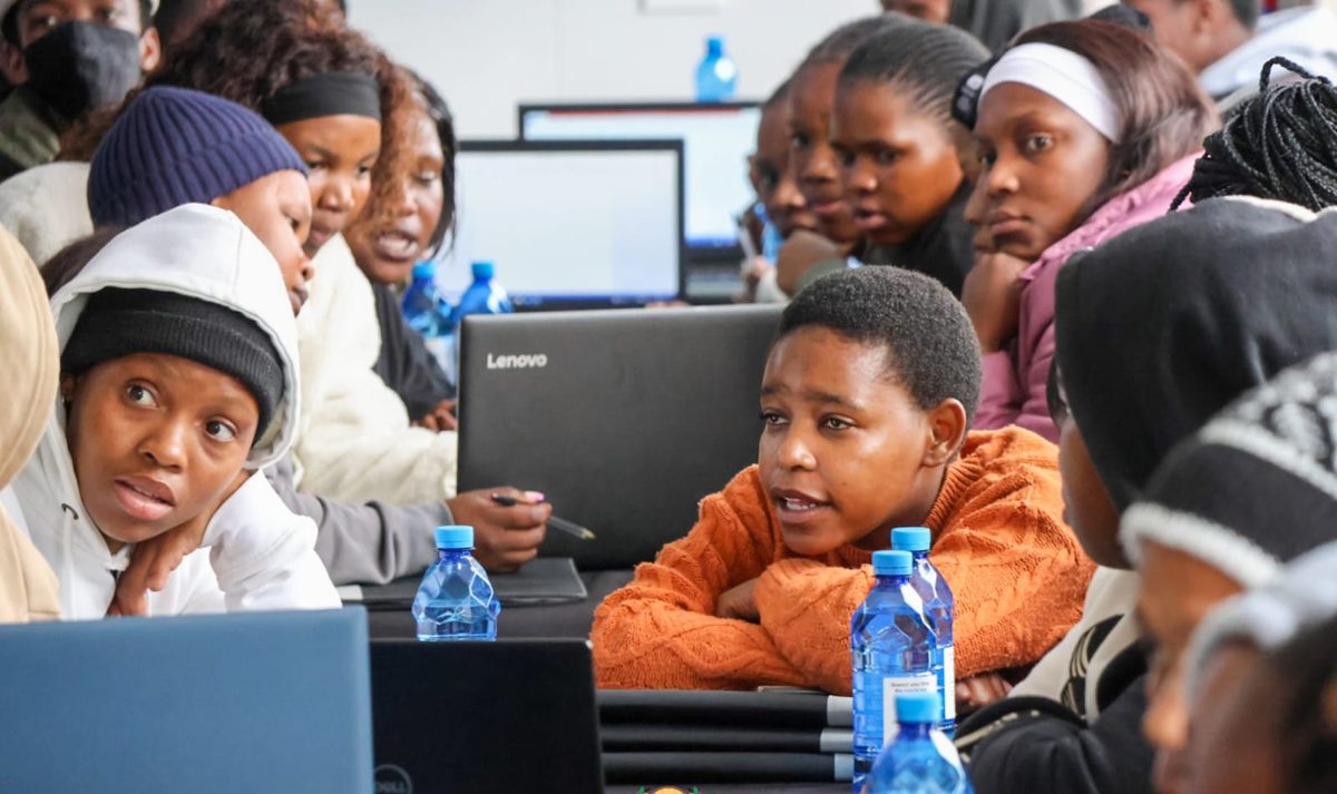 A group of learners gathered around a laptop, talking through a problem together.